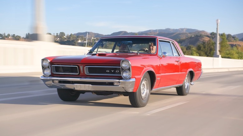 Jay Leno behind the wheel of a red Pontiac GTO Royal Bobcat on the highway