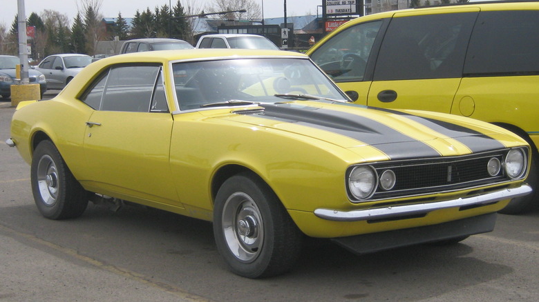 1967 Chevrolet Camaro in yellow with black racing stripes sitting in a parking lot