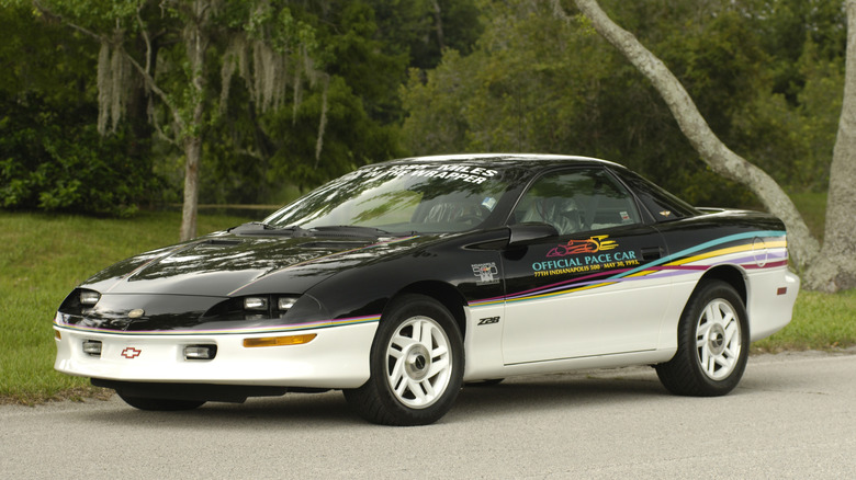 A multi-tone 90s Chevrolet Camaro in Indy 500 Pace Car livery parked outside near trees.