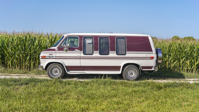 A side-profile view of a 90s Chevy Van parked in front of a corn field.