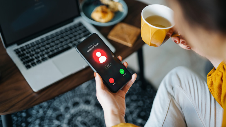 Over the shoulder view of young Asian woman receiving an incoming suspected call from unknown caller on her smartphone and rejecting the call at home