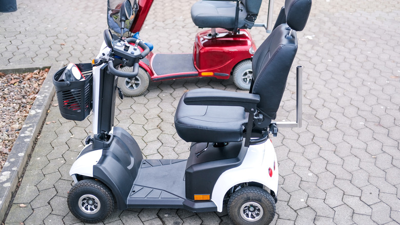 Two mobility scooters sitting outside on pavement