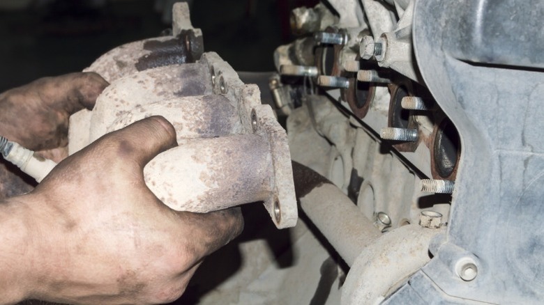a person removing an exhaust manifold from a car