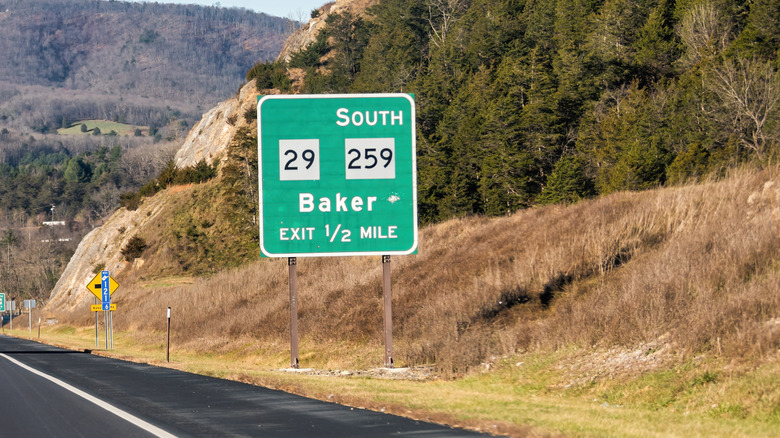 A green south mile marker on the side of a highway with trees in the distance