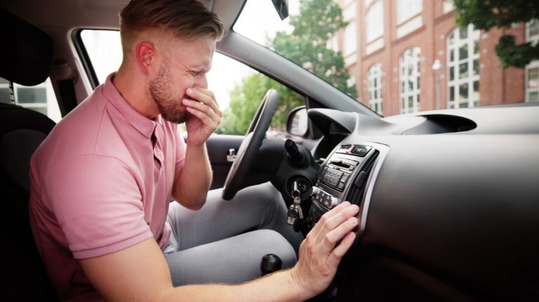 A driver holding their nose due to a bad smell coming from the AC