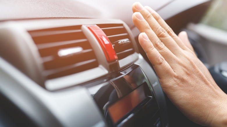 Checking the car's air conditioner vent with an outstretched hand.