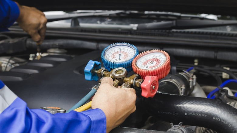 A technician servicing a car's AC using gauges to monitor the system.