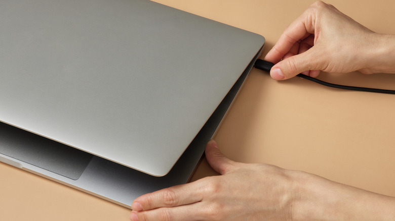 A hand plugging a charging cable into a half-closed laptop