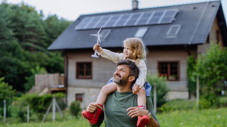 A child and her father in front of a house with solar panels