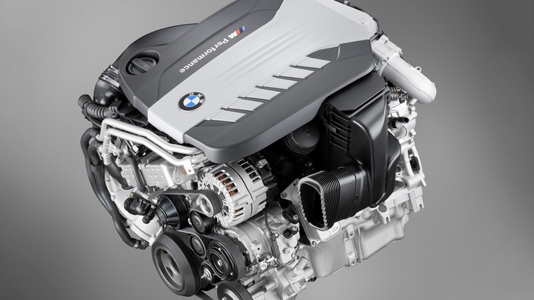 A silver BMW N57 Inline-Six engine model against a slate gray background, top and front view shown.