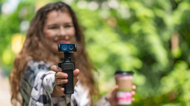A woman holding the Insta360 Luna Ultra in one hand and a cup of coffee in the other.
