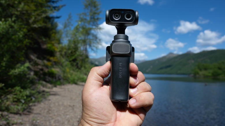 The Insta360 Luna Ultra held in a hand in front of a lake.