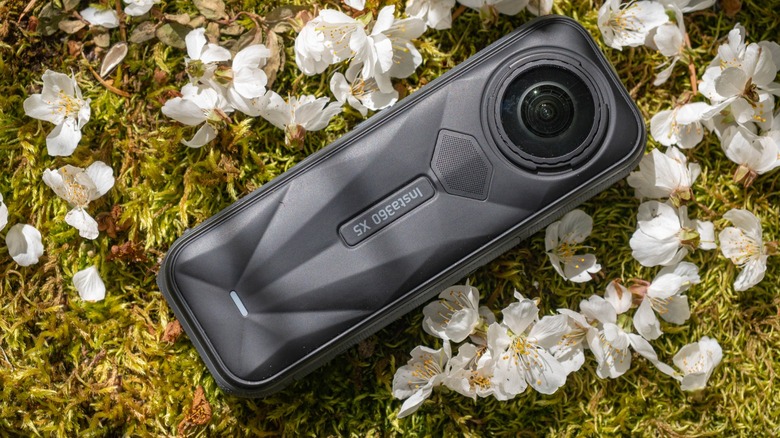 The Insta360 X5 on a bed of moss surrounded by flower petals.