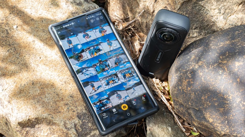 The Insta360 X5 sitting next to a smartphone connected via the Insta360 app showing a selection of clips stored on the camera.
