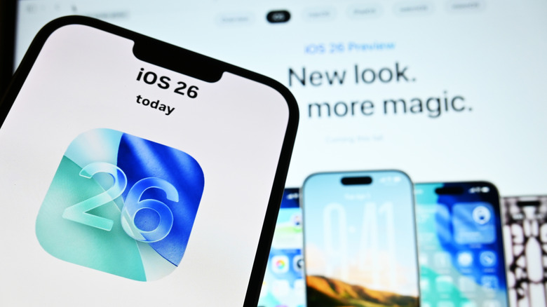 An iPhone with iOS 26 in front of a PC screen showing Apple's website.