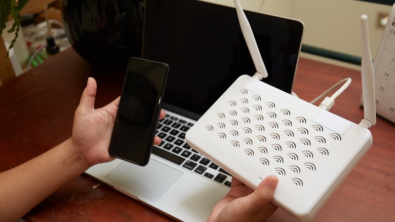 Person holding smartphone and Wi-Fi router