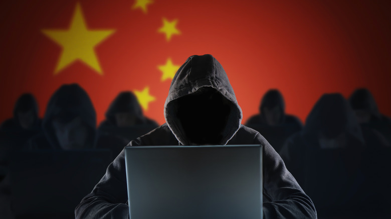 A group of hackers shrouded in shadows browse the web before a Republic of China flag.