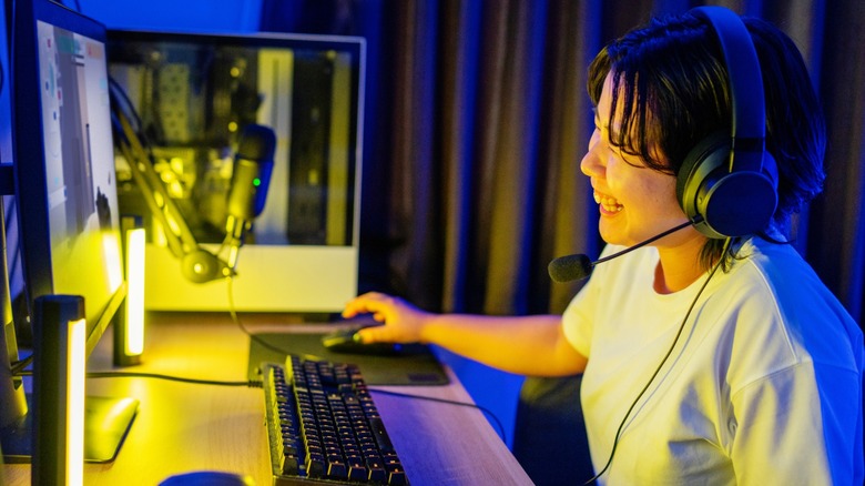 A person laughing while wearing headphones at a desk with a PC and monitor