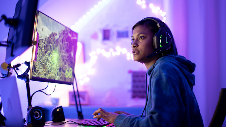 A woman plays video games on a gaming PC with two monitors