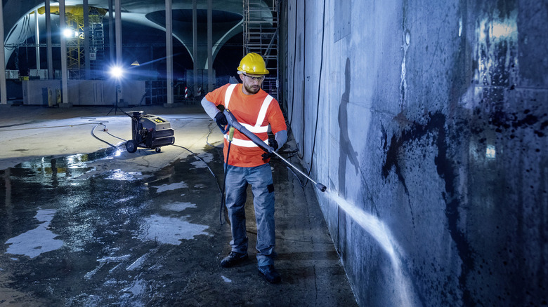 A worker using a hot water pressure washer on a wall