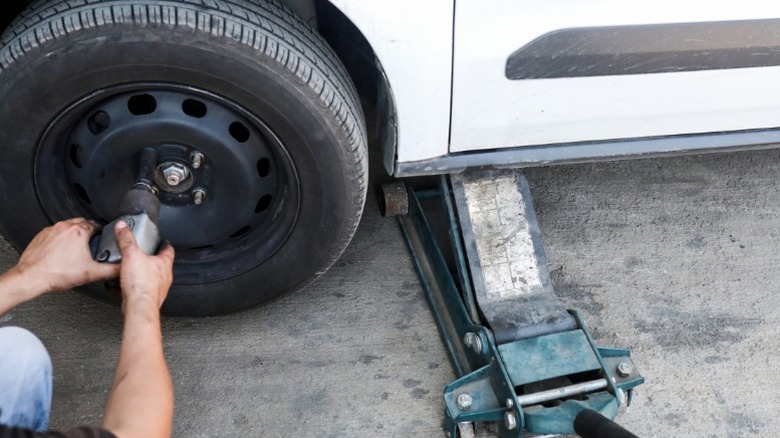 A person removing a wheel from their car after lifting it with a floor jack