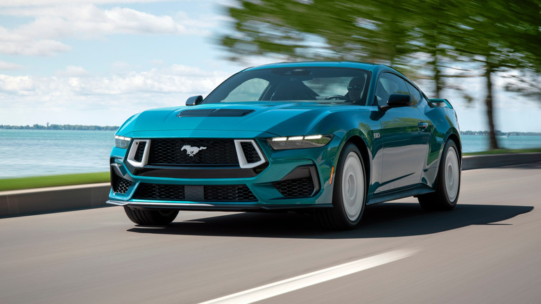 Front 3/4 view of turquoise Ford Mustang GT driving near ocean.
