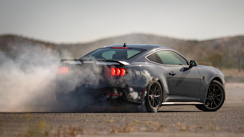 Rear view of Ford Mustang Dark Horse drifting on desert race track.