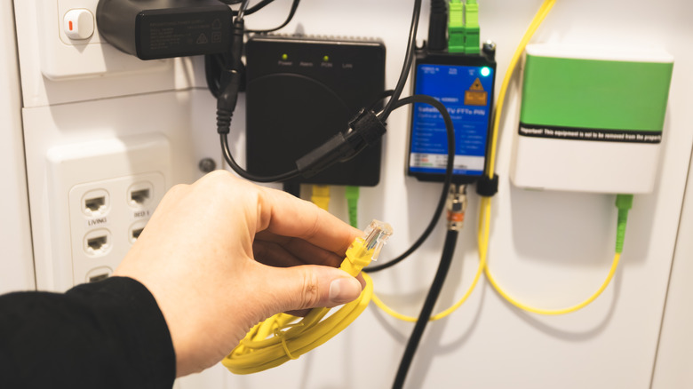A hand holding a yellow ethernet cable near a networking setup