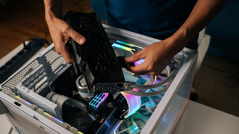 Close up of someone installing a graphics card into a colorfully lit up PC build with a white case