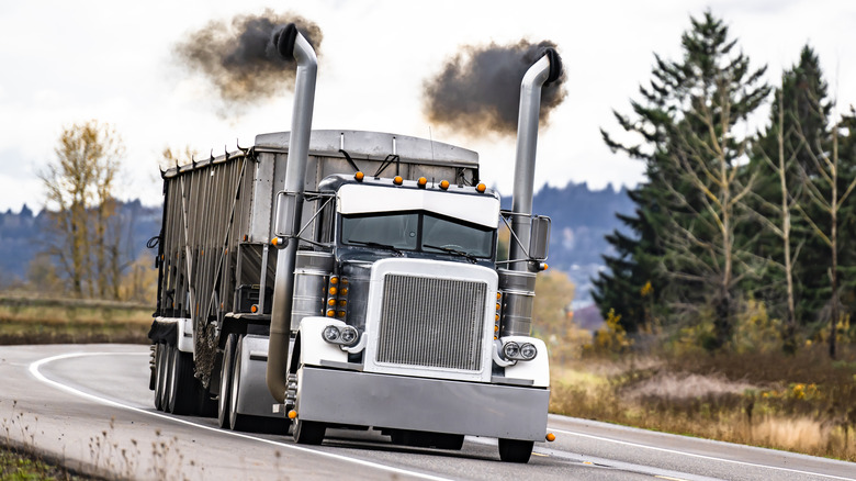 An industrial-grade big rig emits smoke as it churns down the road.