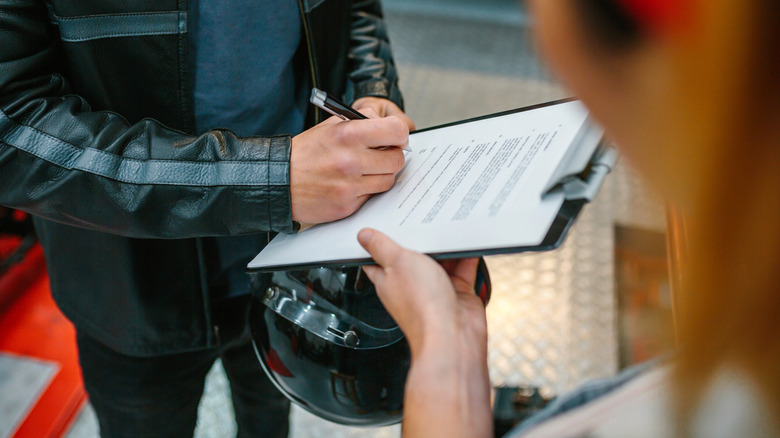 A motorcycle rider signing documents.