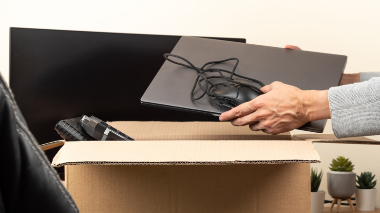 Woman hands put old laptop computer in cardboard box with old used tech gadget devices