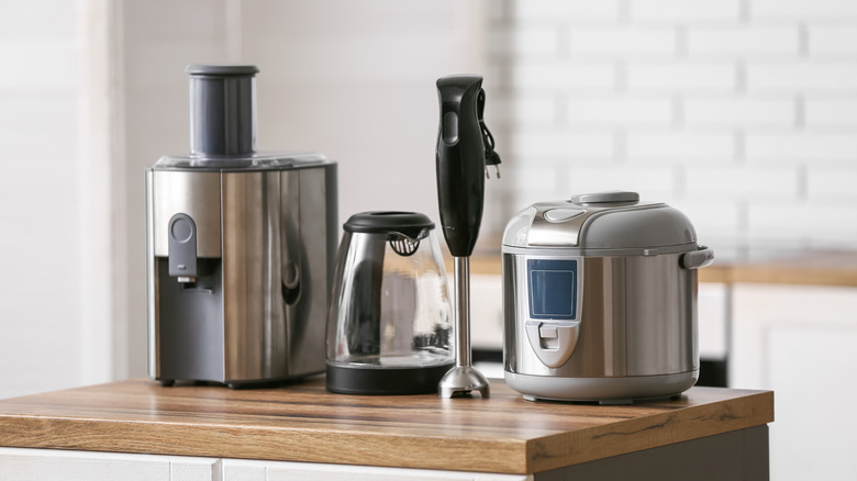 From left to right, a juicer, kettle, immersion blender, and rice cooker lined up on a wooden countertop