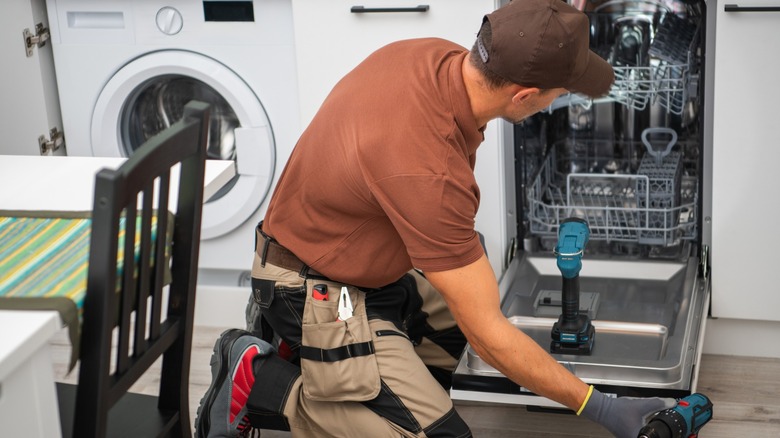 A man works on fixing a dishwasher while kneeling
