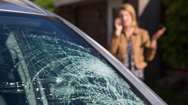Woman calls for help with broken windshield in foreground