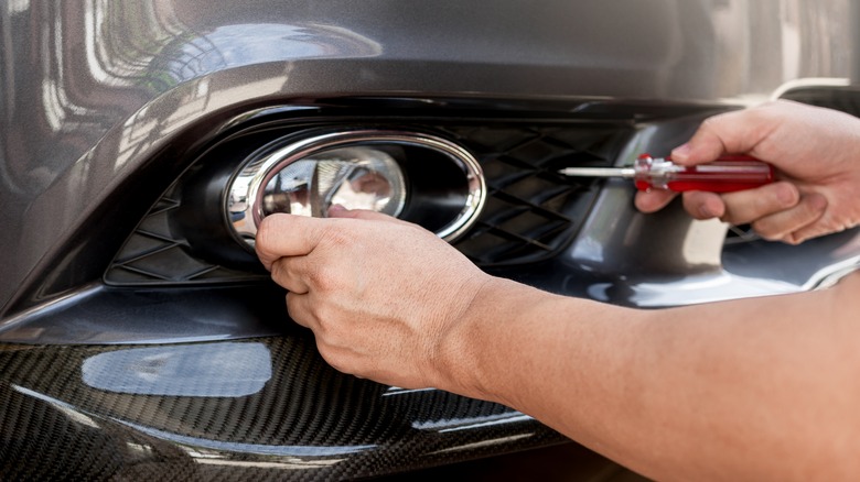 A person adjusting a car's fog lamp with a screwdriver