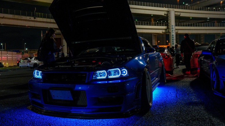A Nissan Skyline R34 with blue neon underglow on display at car show in Daikoku parking area, front view