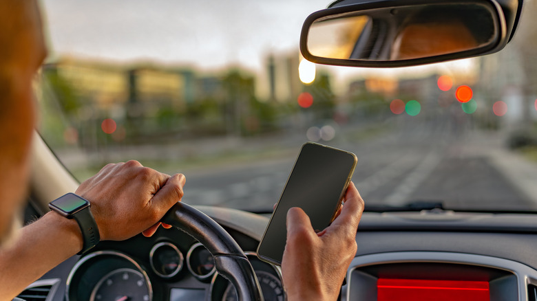 View from inside a vehicle of an adult man using his mobile phone and wearing a smartwatch on one wrist.