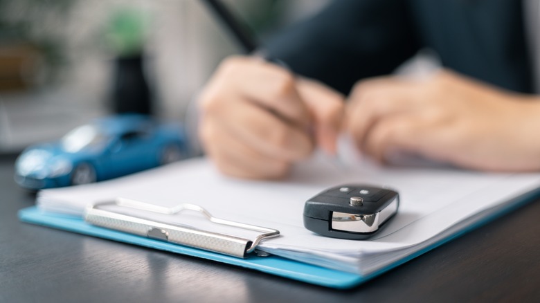 A person signing a contract with a car key in the foreground