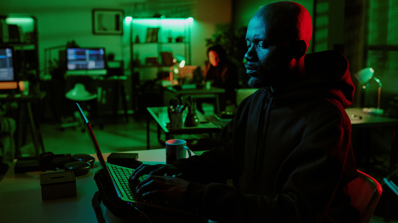 A person using a laptop which is stood on a cooling stand on a desk in a green-lit office.