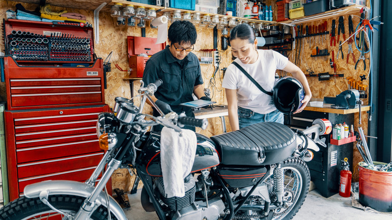 Two people inspecting a motorcycle standing in a workshop