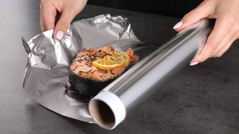 Woman wrapping salmon with lemon and spices in aluminum foil