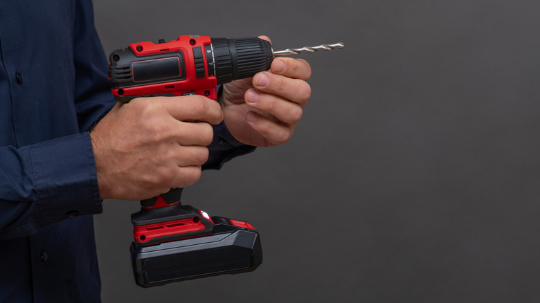 A person in a navy blue shirt adding a drill bit to a cordless drill and preparing to use it