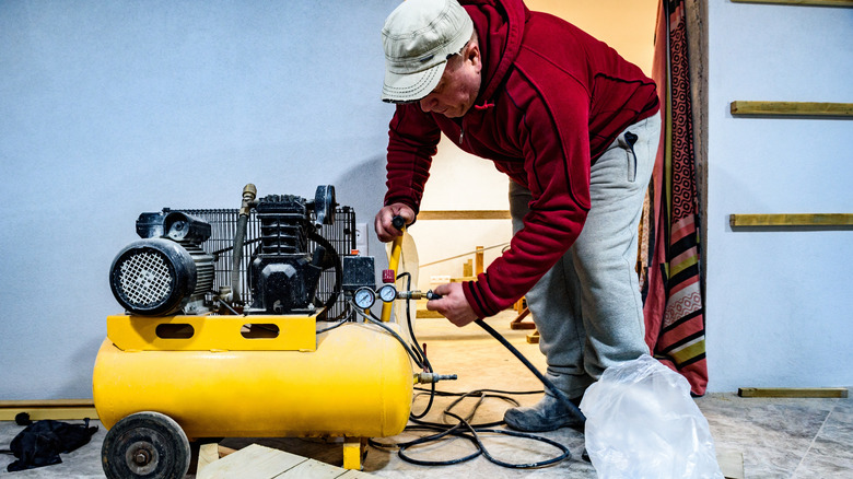 a man starting a yellowish air compressor