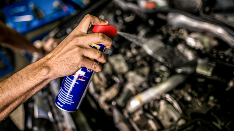 Young auto mechanic cleaning and lubricating car engine with WD-40
