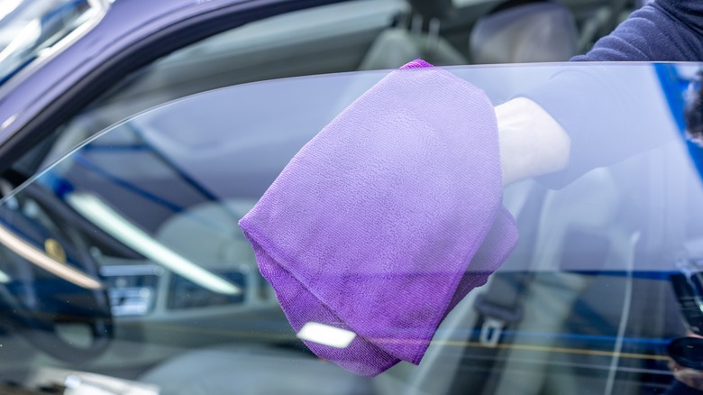 Person wiping the inside of their car window with a purple microfiber cloth