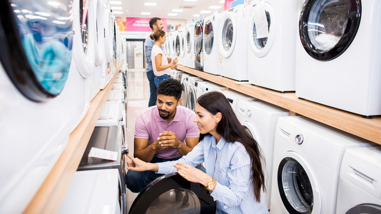 Shoppers checking out washing machines at appliance store.