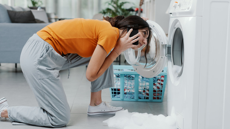 Woman making phone call while inspecting broken washing machine.