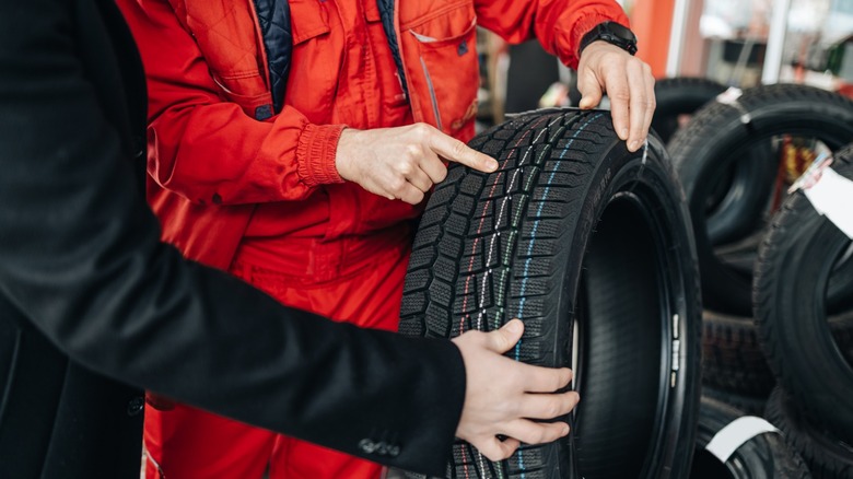 A tire salesman or mechanic showing a new tire to a customer