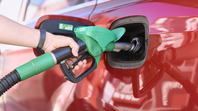A person filling up a red car with gas, close-up shot
